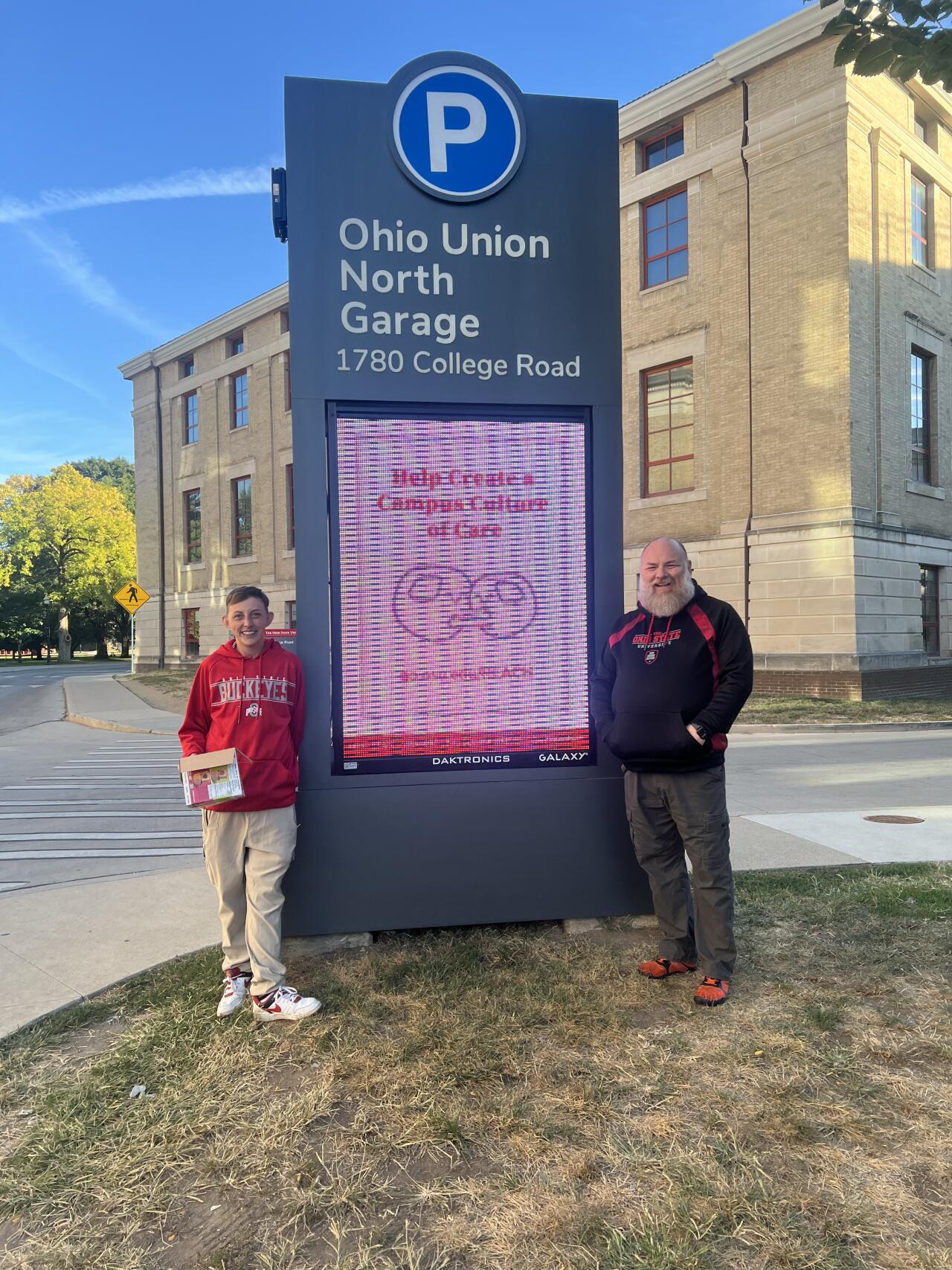 Volunteers at a campus parking garage standing next to a digital parking sign