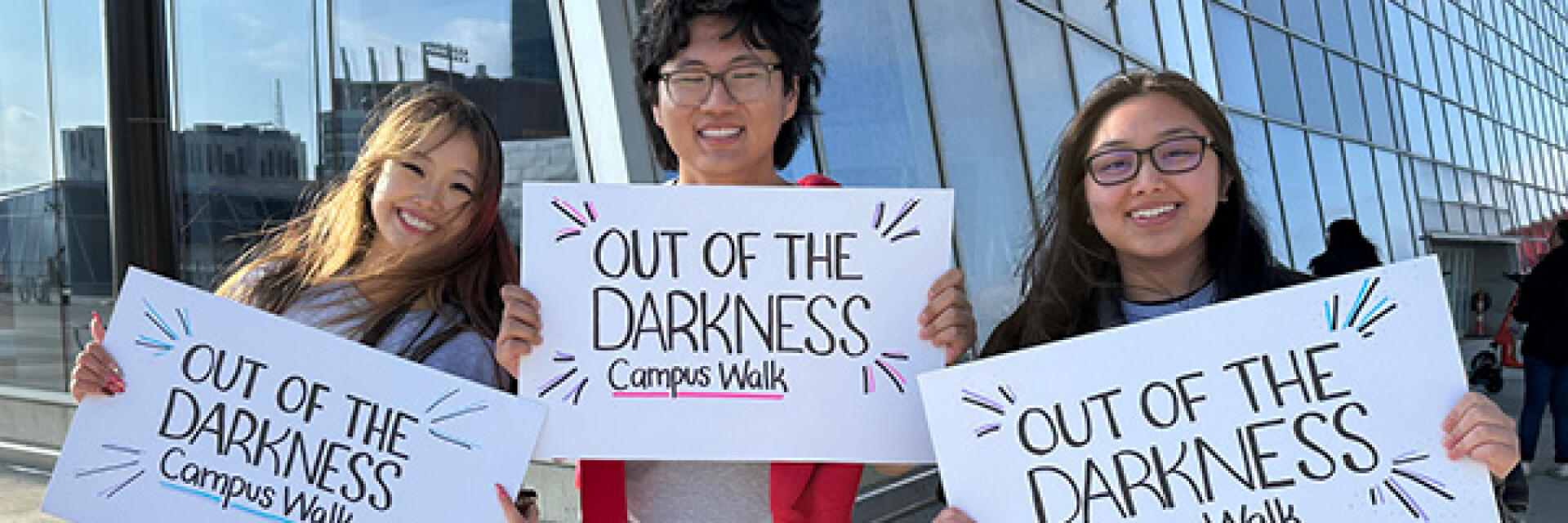 Three people holding up an Out of the Darkness Campus Walk event banner