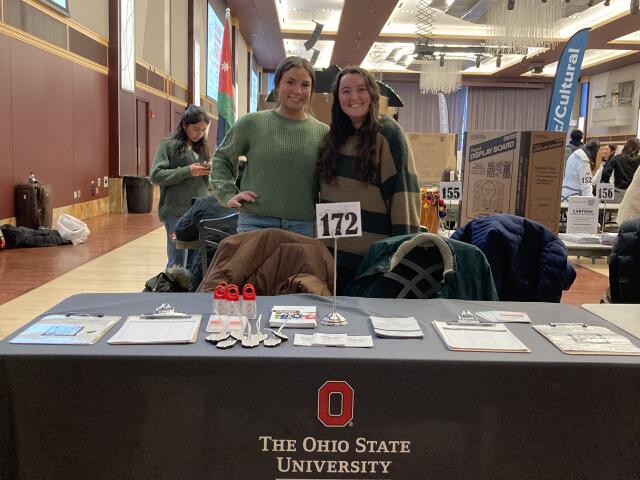 Two students smiling at their booth at an outreach event