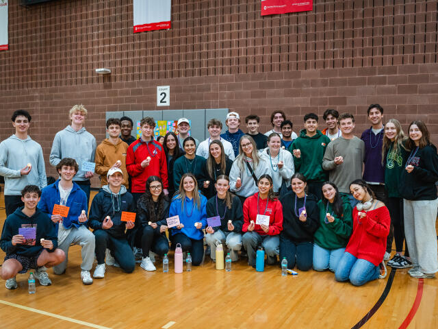 Large group of students holding tealight candles and positive affirmation notes in OSU gym.