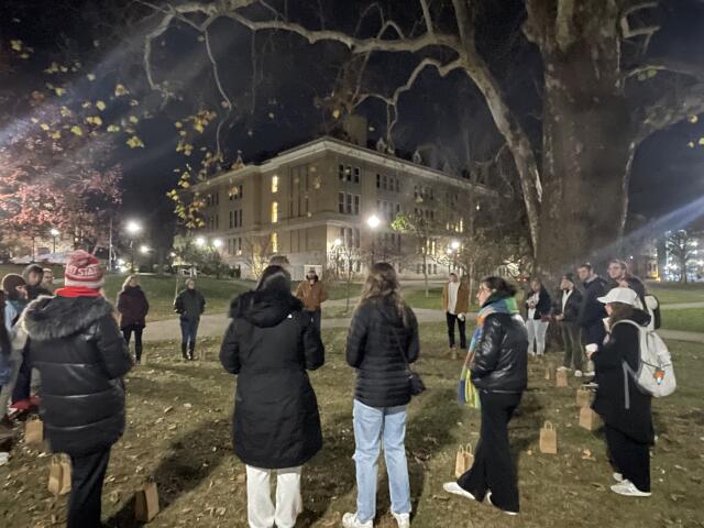 Students gathered together in a circle on a lawn at night time.