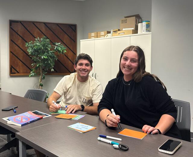 Two students smiling while writing on notecards